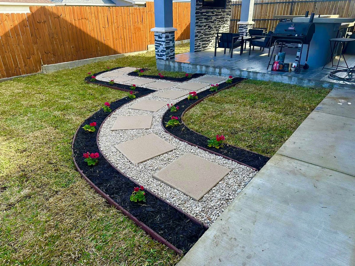 A finished paver pathway with river rock, mulch edging, and red flowers installed by RSR Landscaping in Eagle Pass
